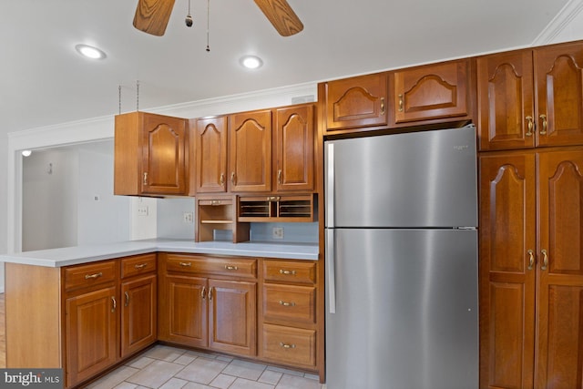 kitchen with light countertops, brown cabinetry, freestanding refrigerator, ceiling fan, and a peninsula