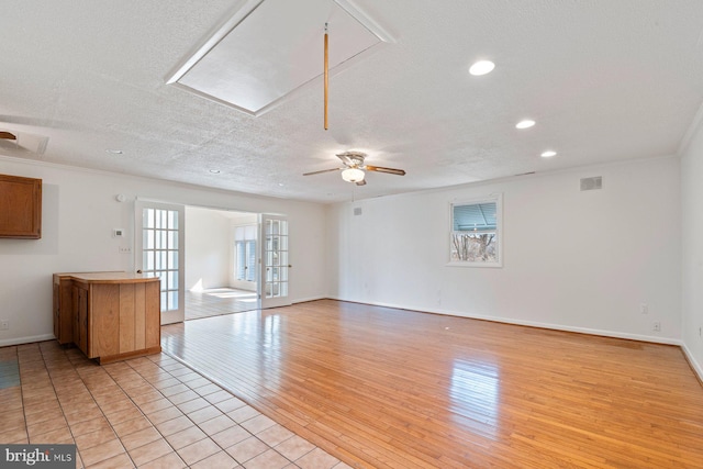 unfurnished living room featuring a textured ceiling, baseboards, light wood-style floors, french doors, and attic access