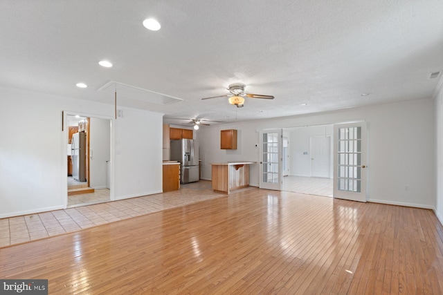 unfurnished living room featuring attic access, baseboards, light wood-style flooring, and french doors