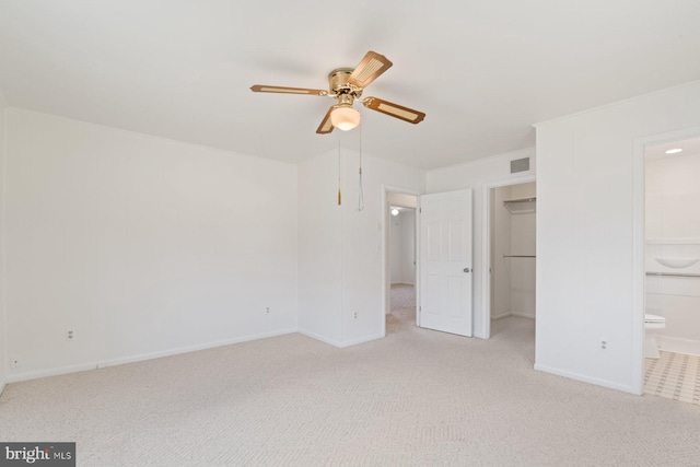 unfurnished bedroom with a walk in closet, visible vents, light carpet, ensuite bath, and baseboards