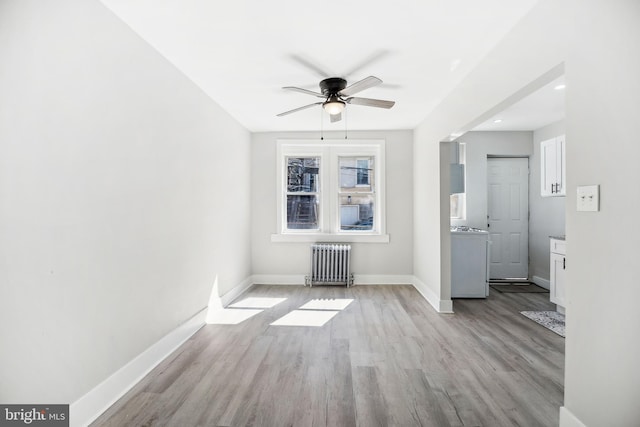 interior space with radiator, a ceiling fan, baseboards, and wood finished floors