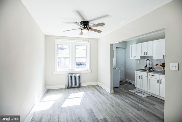 interior space featuring radiator heating unit, decorative backsplash, light wood-style flooring, white cabinets, and a sink