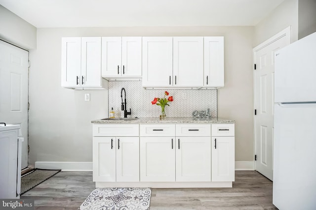 kitchen featuring a sink, light stone counters, backsplash, freestanding refrigerator, and white cabinets