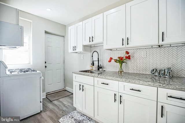 kitchen featuring a sink, light stone counters, gas range oven, white cabinets, and light wood finished floors