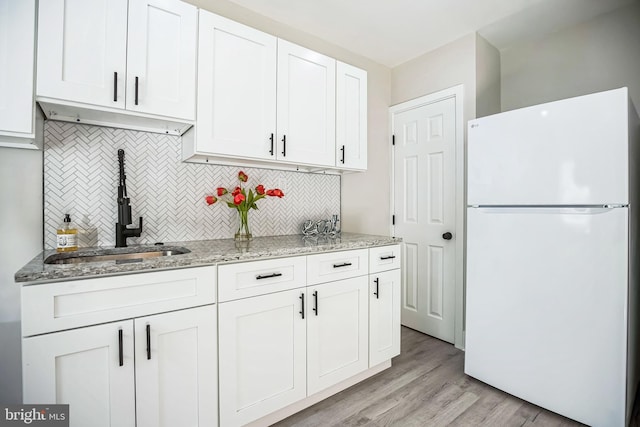 kitchen featuring light wood finished floors, light stone counters, freestanding refrigerator, white cabinetry, and a sink