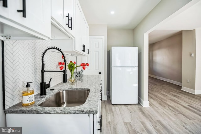 kitchen featuring a sink, white cabinetry, freestanding refrigerator, decorative backsplash, and light stone countertops