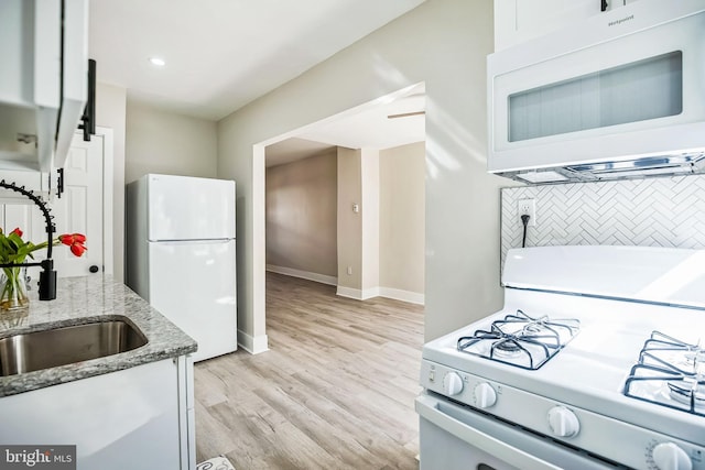 kitchen with light wood-type flooring, light stone counters, tasteful backsplash, white cabinetry, and white appliances