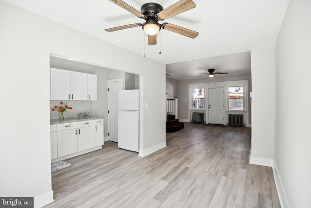 kitchen featuring light wood-type flooring, radiator, white cabinets, and freestanding refrigerator