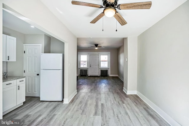 interior space with baseboards, white cabinetry, radiator heating unit, and freestanding refrigerator