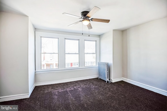 spare room featuring dark carpet, radiator, baseboards, and ceiling fan