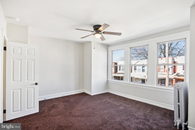 empty room with radiator, baseboards, dark carpet, and ceiling fan