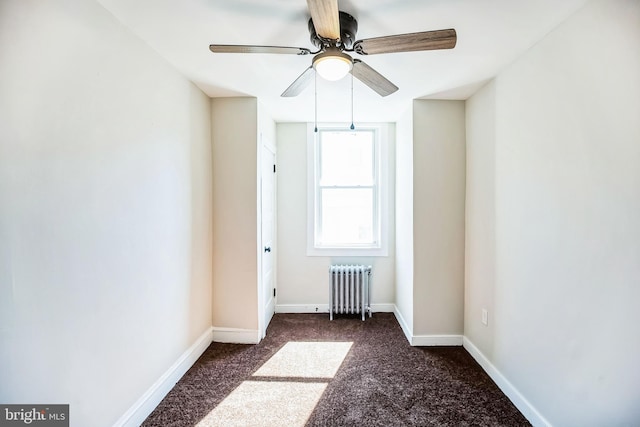 unfurnished room featuring dark carpet, radiator, baseboards, and ceiling fan