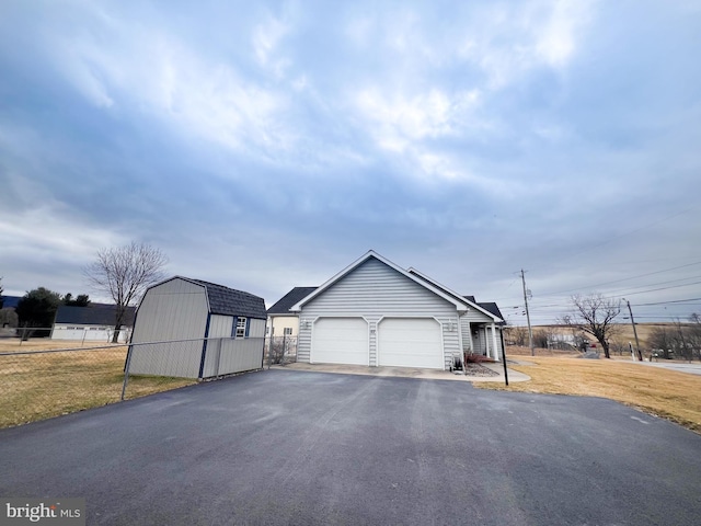 garage featuring a storage unit, fence, and aphalt driveway