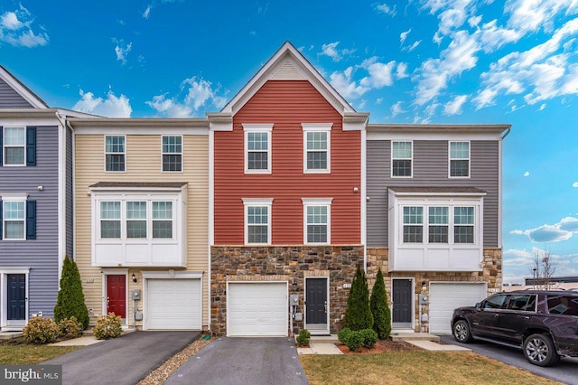 multi unit property with driveway, stone siding, and a garage