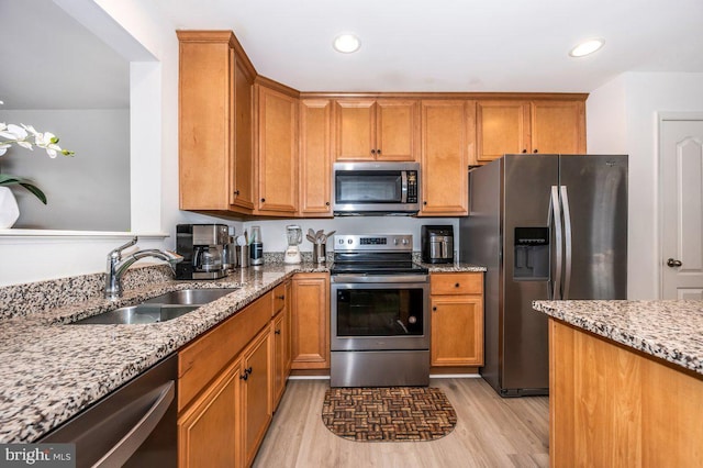 kitchen featuring light stone counters, stainless steel appliances, a sink, brown cabinets, and light wood finished floors