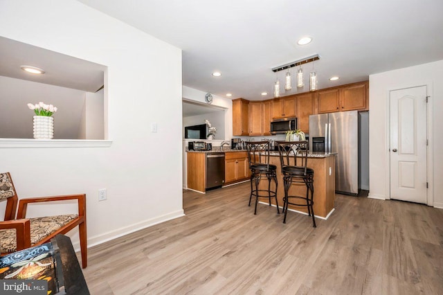 kitchen featuring appliances with stainless steel finishes, brown cabinetry, light wood finished floors, and a breakfast bar area