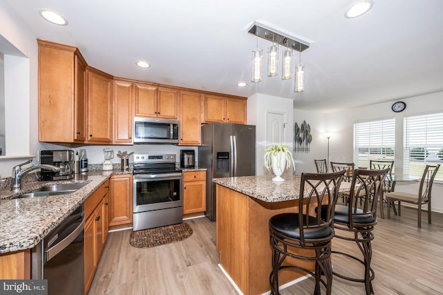 kitchen featuring brown cabinetry, light wood-style flooring, stainless steel appliances, and a sink