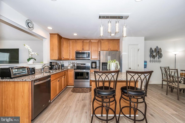 kitchen with a breakfast bar, light wood-style floors, light stone counters, and stainless steel appliances