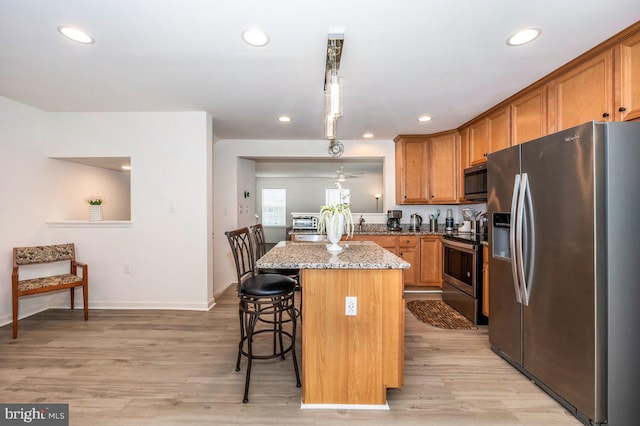 kitchen with light wood-style flooring, stainless steel appliances, a breakfast bar, brown cabinets, and light stone countertops