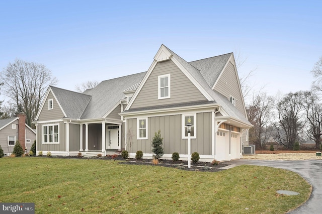 view of front of home with a front yard, central AC unit, driveway, an attached garage, and board and batten siding