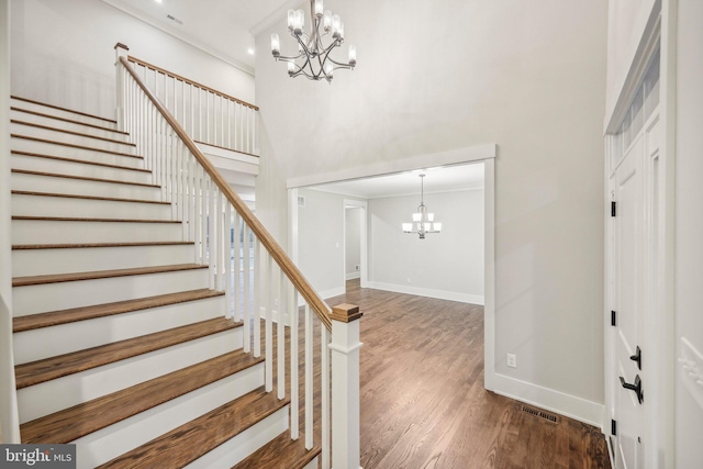 foyer entrance with wood finished floors, baseboards, ornamental molding, a towering ceiling, and a chandelier