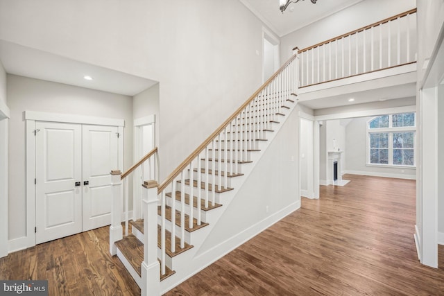 stairway with a fireplace with flush hearth, a high ceiling, baseboards, and wood finished floors