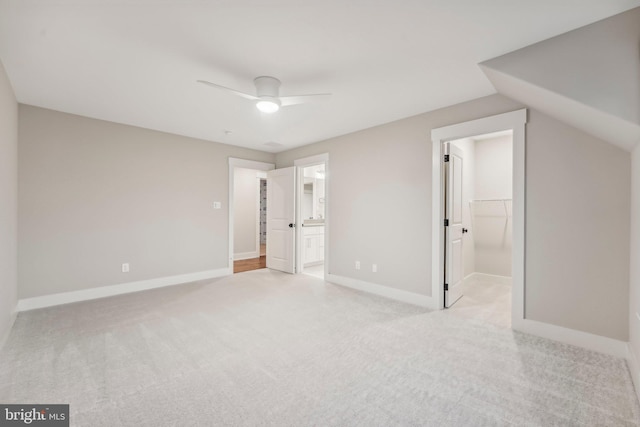 unfurnished bedroom featuring a spacious closet, baseboards, lofted ceiling, light carpet, and ensuite bathroom