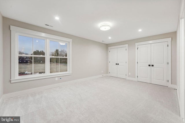 unfurnished bedroom featuring visible vents, multiple closets, light carpet, recessed lighting, and baseboards