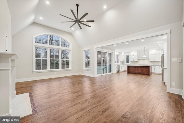 unfurnished living room featuring lofted ceiling, wood finished floors, baseboards, and ceiling fan