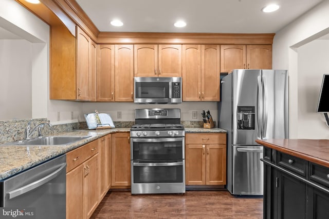 kitchen with light stone counters, recessed lighting, a sink, appliances with stainless steel finishes, and dark wood finished floors