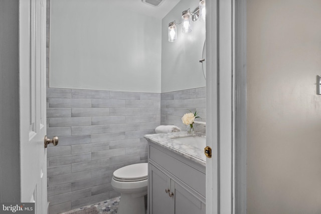 bathroom featuring toilet, a wainscoted wall, vanity, and tile walls