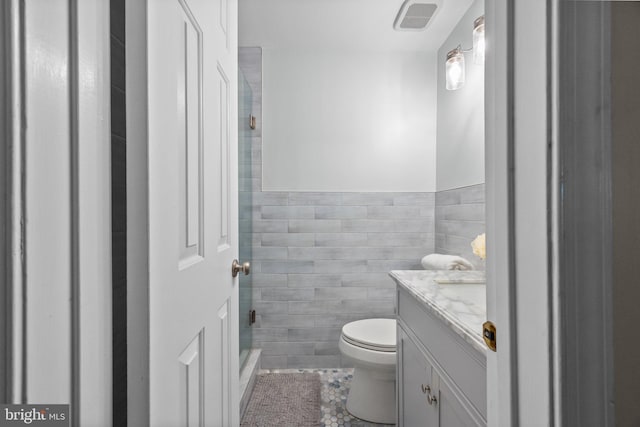 bathroom featuring visible vents, a shower, toilet, vanity, and tile walls