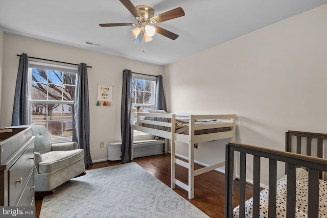 bedroom with a ceiling fan, dark wood-style flooring, visible vents, and baseboards