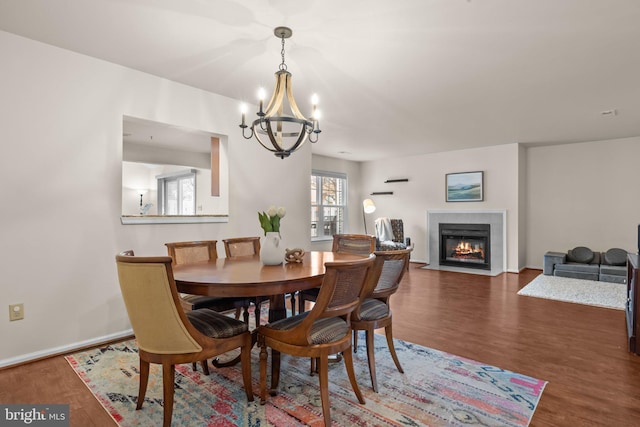 dining space with a chandelier, baseboards, a tiled fireplace, and wood finished floors