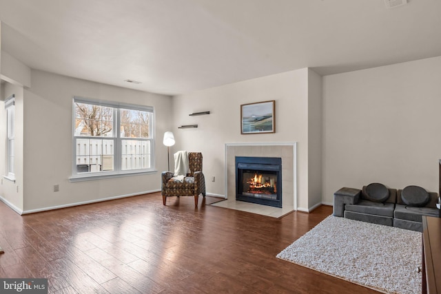 sitting room with a tile fireplace, visible vents, baseboards, and wood finished floors