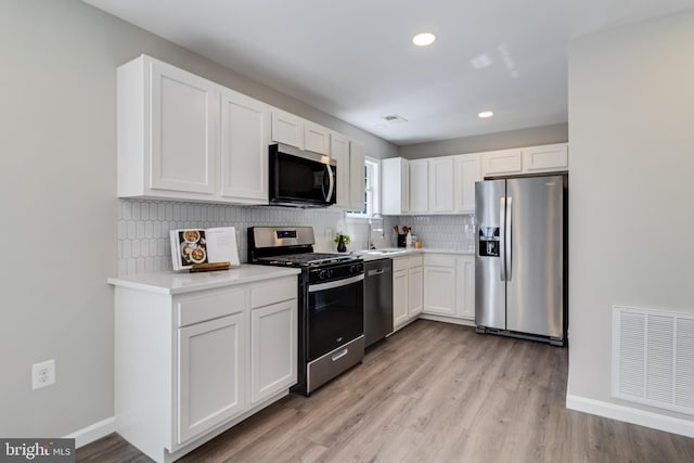 kitchen featuring tasteful backsplash, visible vents, stainless steel appliances, light wood-style floors, and white cabinetry