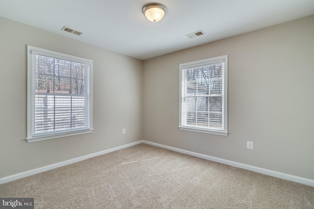 carpeted empty room featuring visible vents, a healthy amount of sunlight, and baseboards