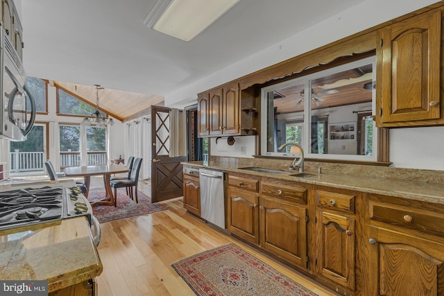 kitchen featuring lofted ceiling, decorative light fixtures, stainless steel appliances, light wood-type flooring, and a sink