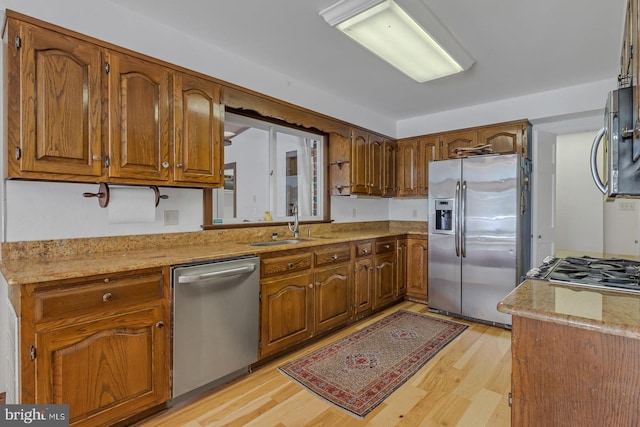 kitchen with appliances with stainless steel finishes, light wood-style floors, brown cabinetry, and a sink