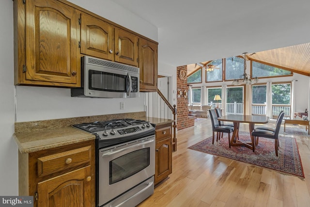 kitchen with brown cabinetry, lofted ceiling, appliances with stainless steel finishes, light countertops, and light wood-type flooring