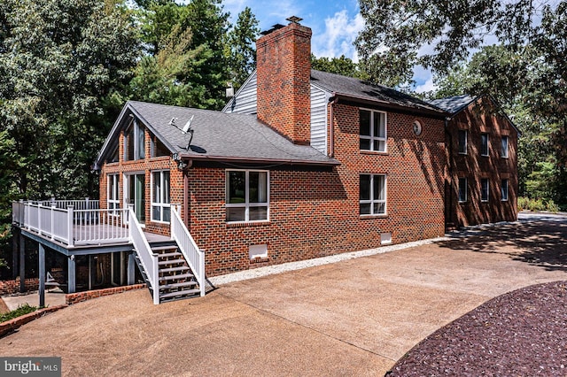 back of house with brick siding, a chimney, a shingled roof, crawl space, and stairs