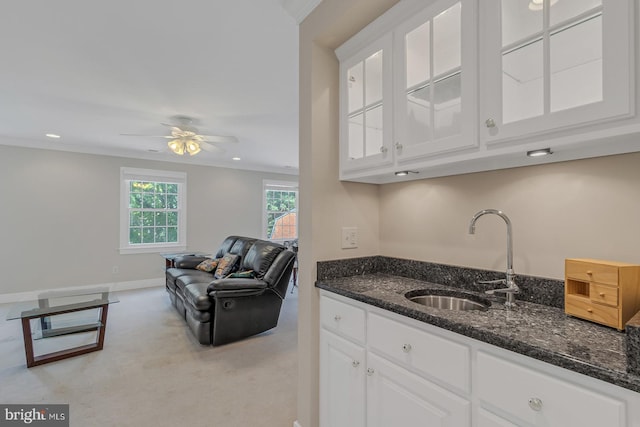 kitchen featuring a sink, white cabinets, open floor plan, ornamental molding, and dark stone countertops