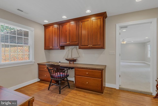 office space with baseboards, built in desk, visible vents, and light wood-style floors