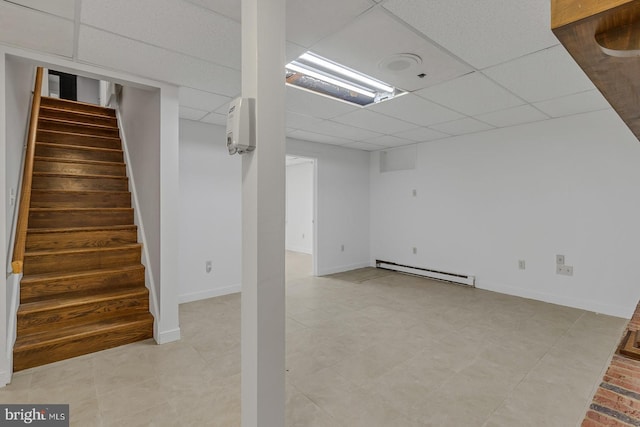 finished basement featuring a baseboard radiator, stairway, a wall mounted AC, a drop ceiling, and baseboards