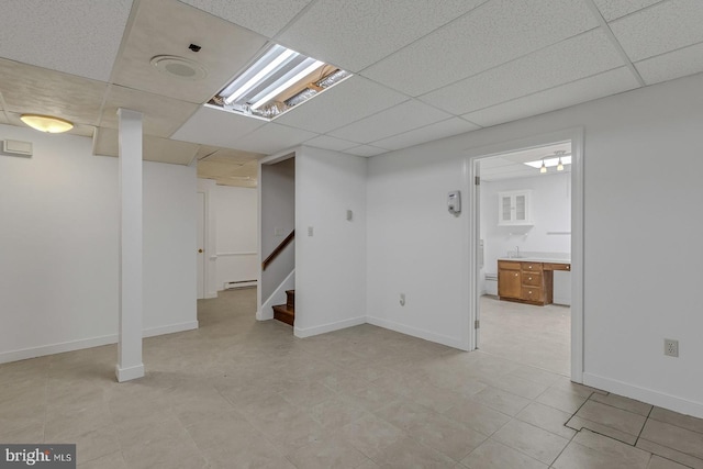 finished below grade area featuring a paneled ceiling, baseboards, and stairs