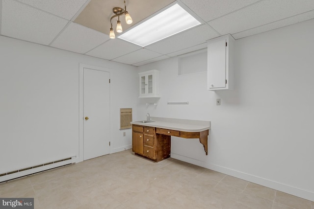 unfurnished office with a baseboard radiator, baseboards, a paneled ceiling, and a sink