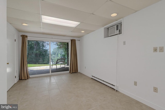 spare room with a baseboard heating unit, an AC wall unit, a drop ceiling, and baseboards