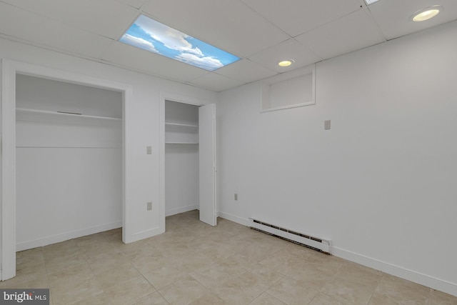 unfurnished bedroom featuring a drop ceiling, a baseboard radiator, two closets, and baseboards