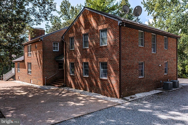 view of side of property featuring a chimney, central AC unit, and brick siding