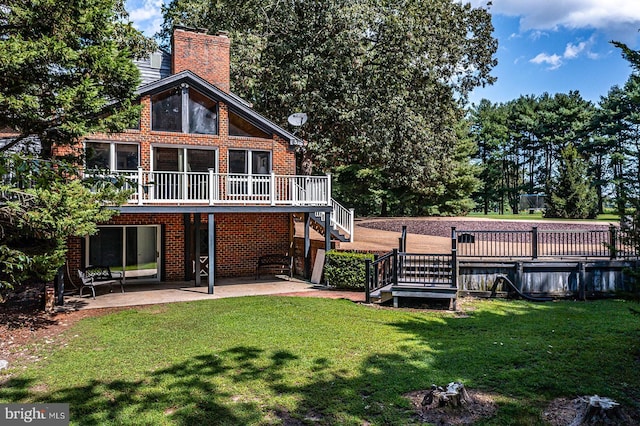 back of house with a deck, brick siding, stairs, a lawn, and a chimney